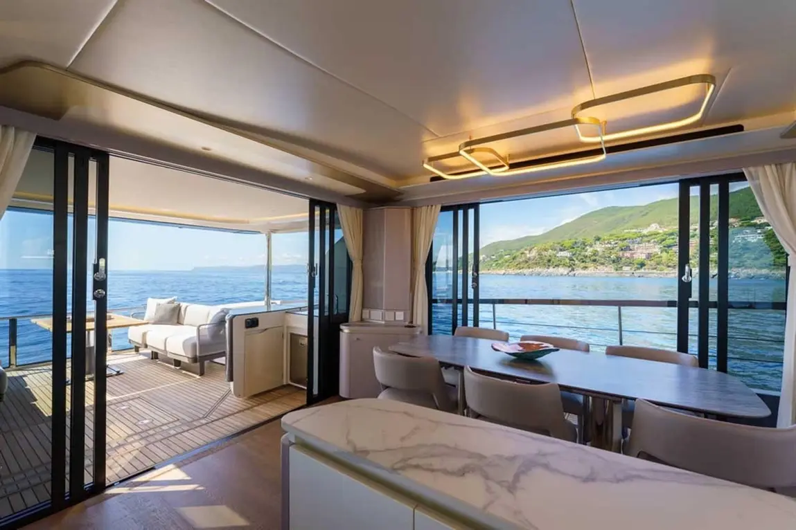 Luxury yacht interior with open view, featuring a dining area, lounge, and ocean scenery through glass doors.
